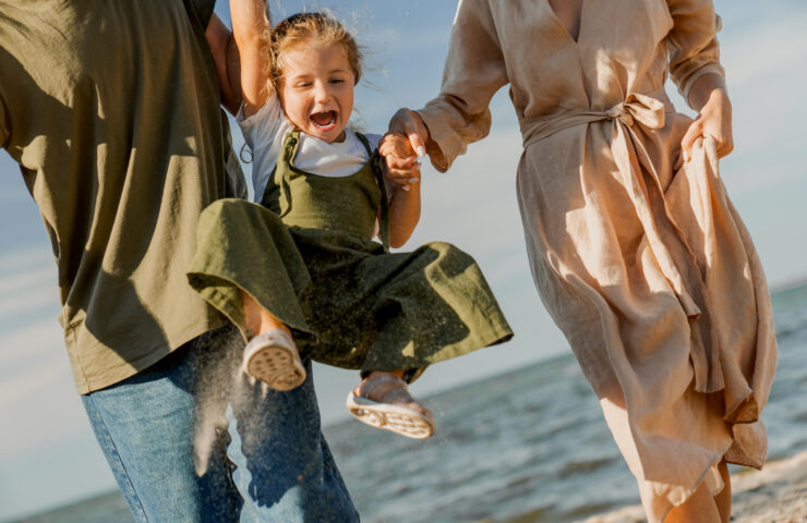 Cropped shot of happy family walking and having fun on the beach with happy cute girl