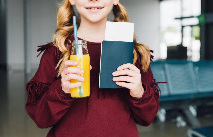 Cropped view of preteen kid with air ticket, passport and orange juice in airport