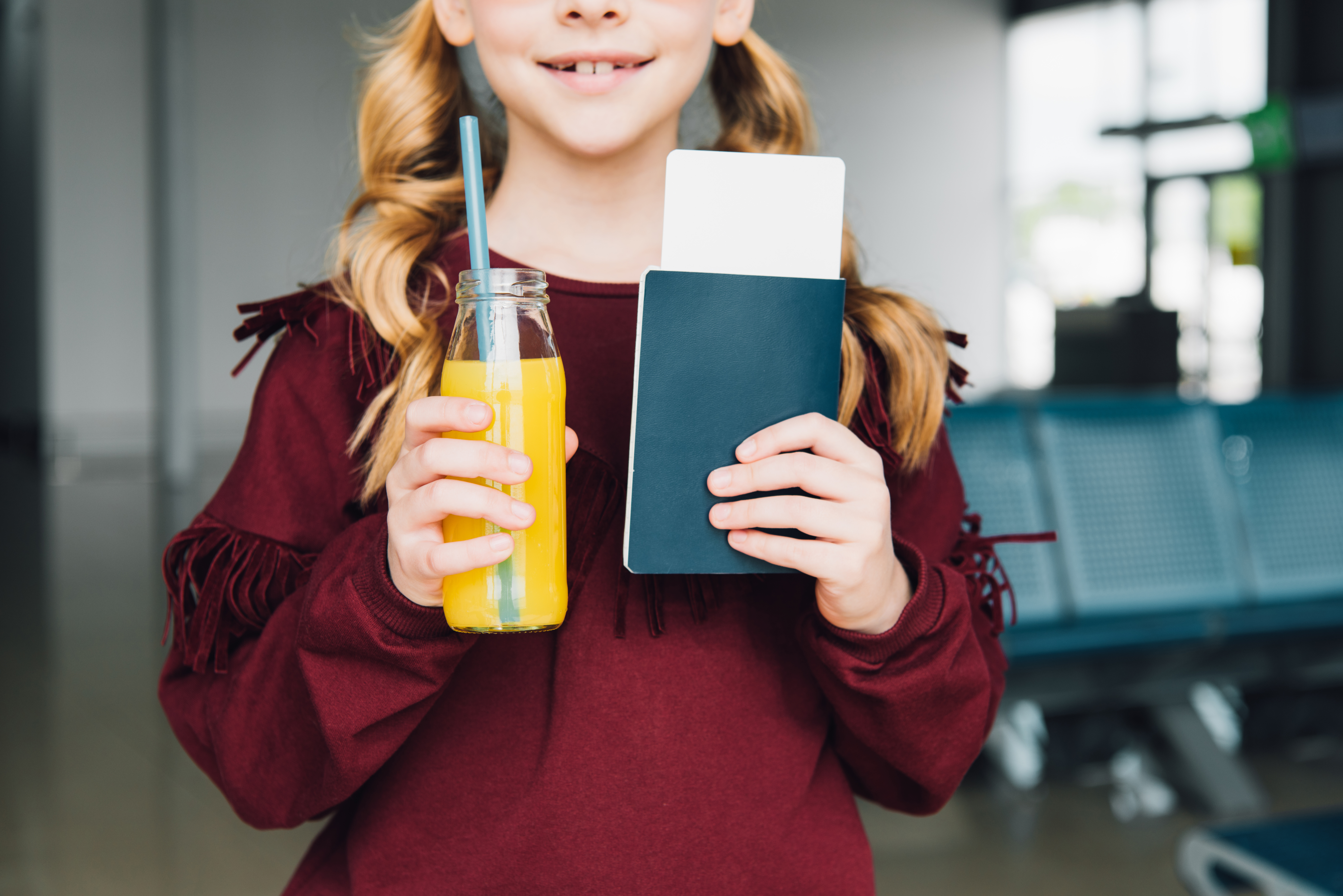 Cropped view of preteen kid with air ticket, passport and orange juice in airport