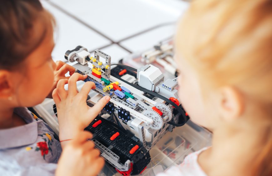 Two schoolgirls study in a robotics class, assemble a robot constructor
