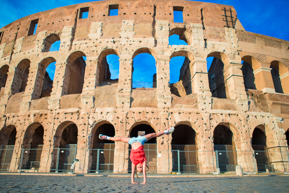 Adorable little active girl having fun in front of colosseum in rome, italy