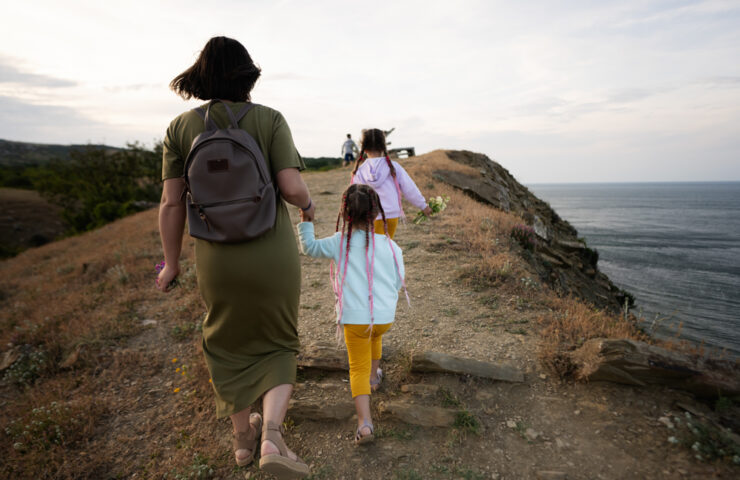 Back view of mother and children walking on cliff near sea at su