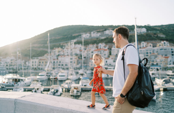 Dad walks along the boardwalk holding the hand of his little daughter walking along the curb