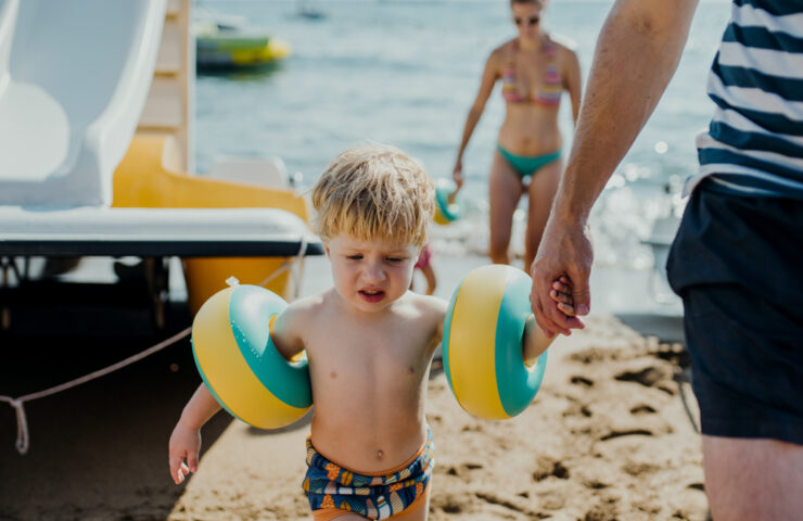 Family with two small toddler children walking on beach on summer holiday.
