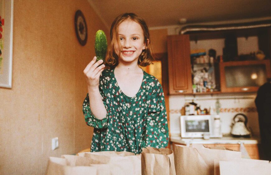 happy-girl-showing-cucumber-in-kitchen-2025-01-09-02-25-11-utc