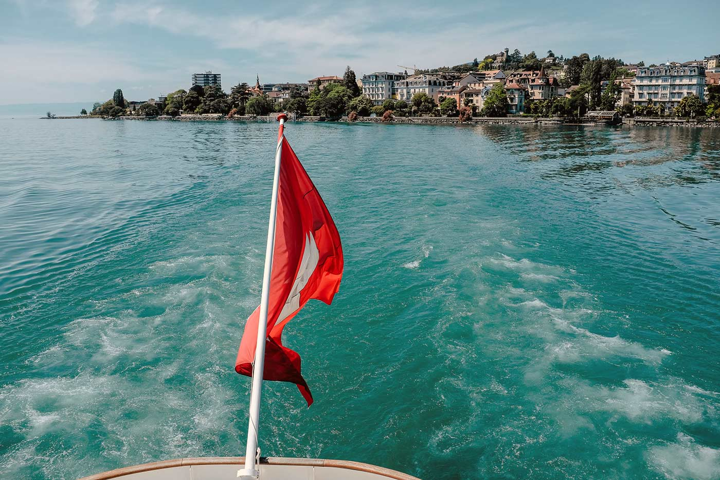 a-red-flag-on-a-boat-with-old-buildings-and-lush-n-2025-10-17-07-17-18-utc